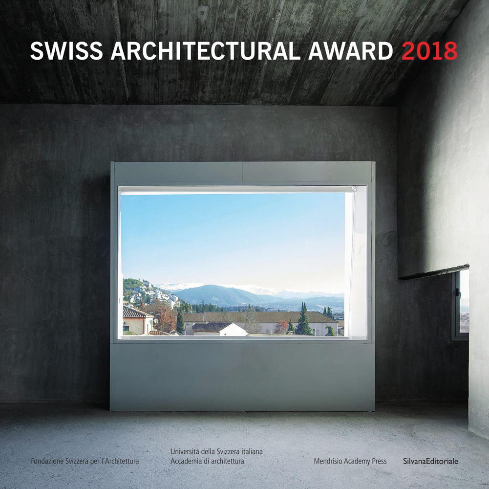 View of mountainous landscape from interior window inside grey room, Swiss Architectural Award 2018 in white and red font above