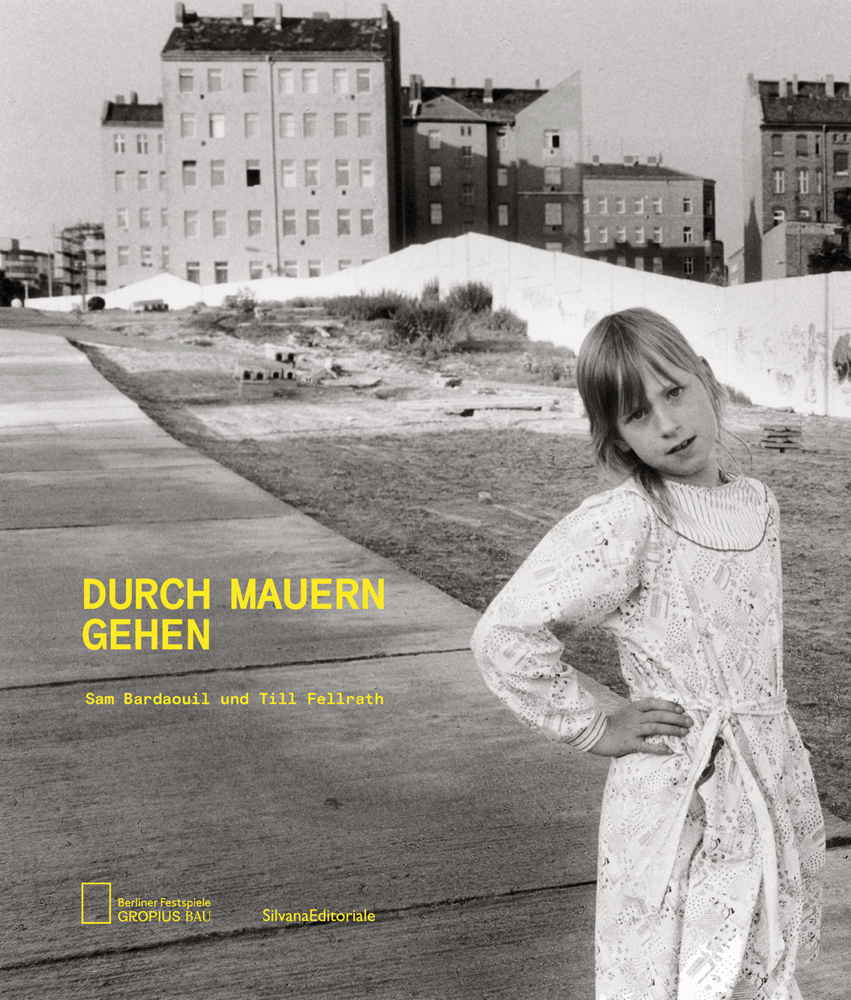 Young girl, hand on hip, in long white dress, urban buildings with long white wall behind, DURCH MAUREN GEHEN in yellow font to lower left.