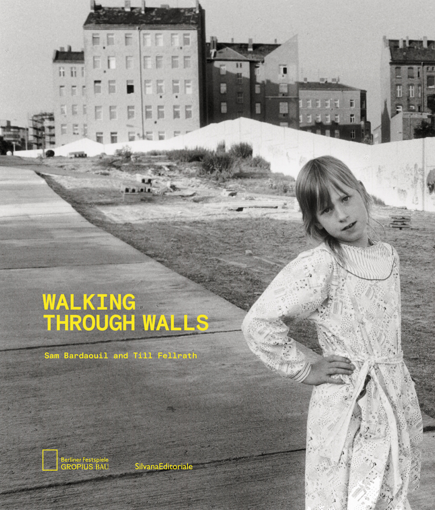 Young girl, hand on hip, in long white dress, urban buildings with long white wall behind, WALKING THROUGH WALLS in yellow font to lower left.