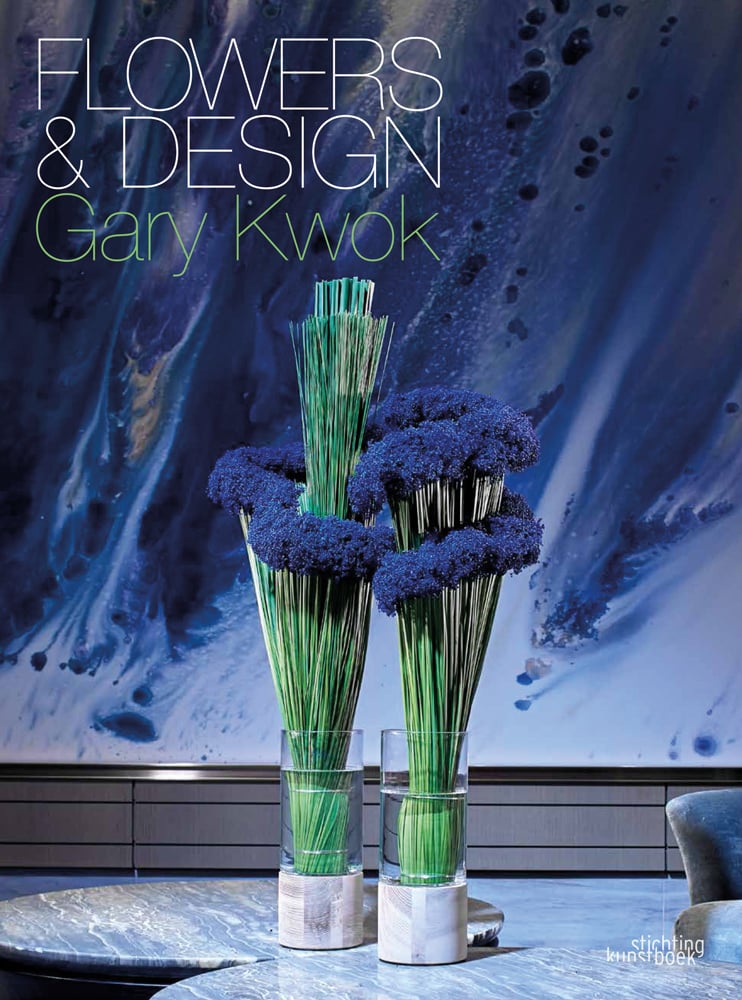 2 glass holders with thin green stems topped with tiny bright blue flower, on blue marble cover, Flowers and Design in white font