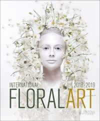 White book cover of International Floral Art 2018/2019, with a model wearing white face paint, and a head-dress of white flowers cascading down. Published by Stichting.