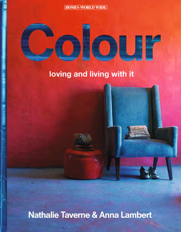 Blue armchair with a stack of papers on seat, pair of heeled shoes underneath with large red pot on floor, on cover of 'Colour Loving it and living with It', by Lannoo Publishers.