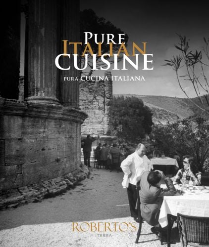 Outside restaurant table with two people taking to man in chef whites, near Italian ruins, on cover of 'Pure Italian Cuisine, Roberto's', by Lannoo Publishers.
