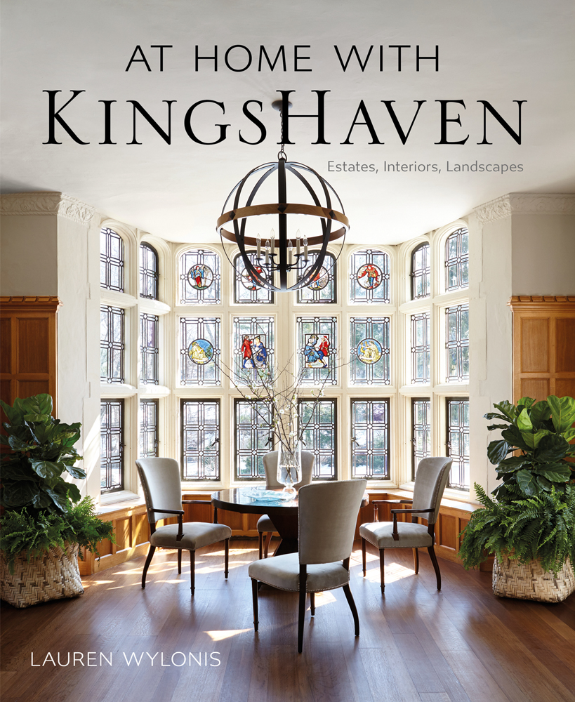 Light interior space, wood floor, table and chairs in front of large stained glass window, AT HOME WITH KINGSHAVEN in black font above.