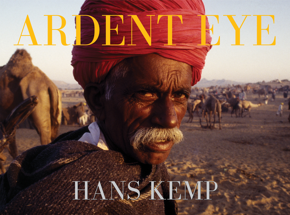 Dark skinned man in red turban standing in desert, camel behind, ARDENT EYE HAN KEMP in yellow and lilac font above and below.