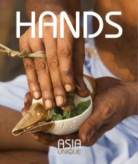 Book cover of Hands, Asia Unique, featuring the hands of Asian male holding white and gold shell, stuffed with green leaves tied together. Published by Visionary World.