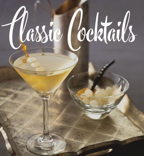 Cocktail glass with yellow liquid, cocktail stick holding small onions, on gold covered wood tray, Classic Cocktails in white font above.