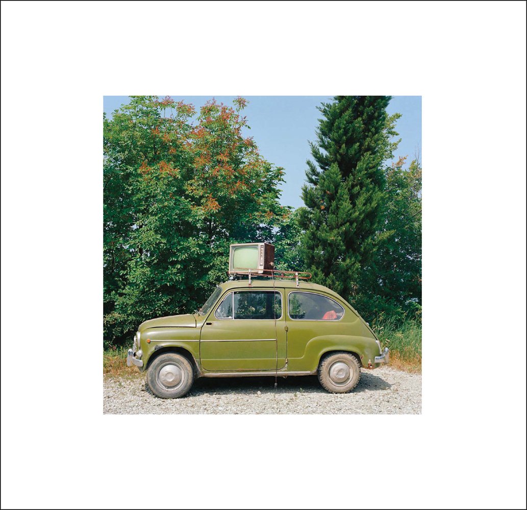 Book cover of Olivo Barbieri's Early Works: 1980 - 1984, with a green Fiat 500 with a T.V strapped to the roof, large green trees behind. Published by L'Artiere.