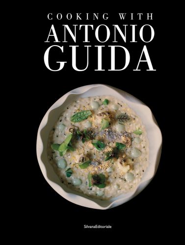 Aerial view of wavy edged bowl filled with broad bean risotto with herb leaves on top, black cover, COOKING WITH ANTONIO GUIDA in white font above.