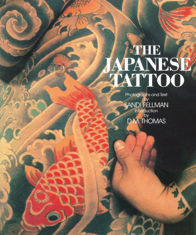 Tattoo on chest of male, of red Japanese koi fish, surrounded by black and white waves, THE JAPANESE TATTOO in white font to upper right.