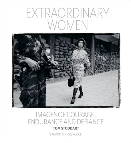 Black and white landscape photograph of a women in a dress and heels walking towards a person in camouflage clothes holding a gun their head and feet obscured with Extraordinary Women Images of Courage, Endurance & Defiance in grey font