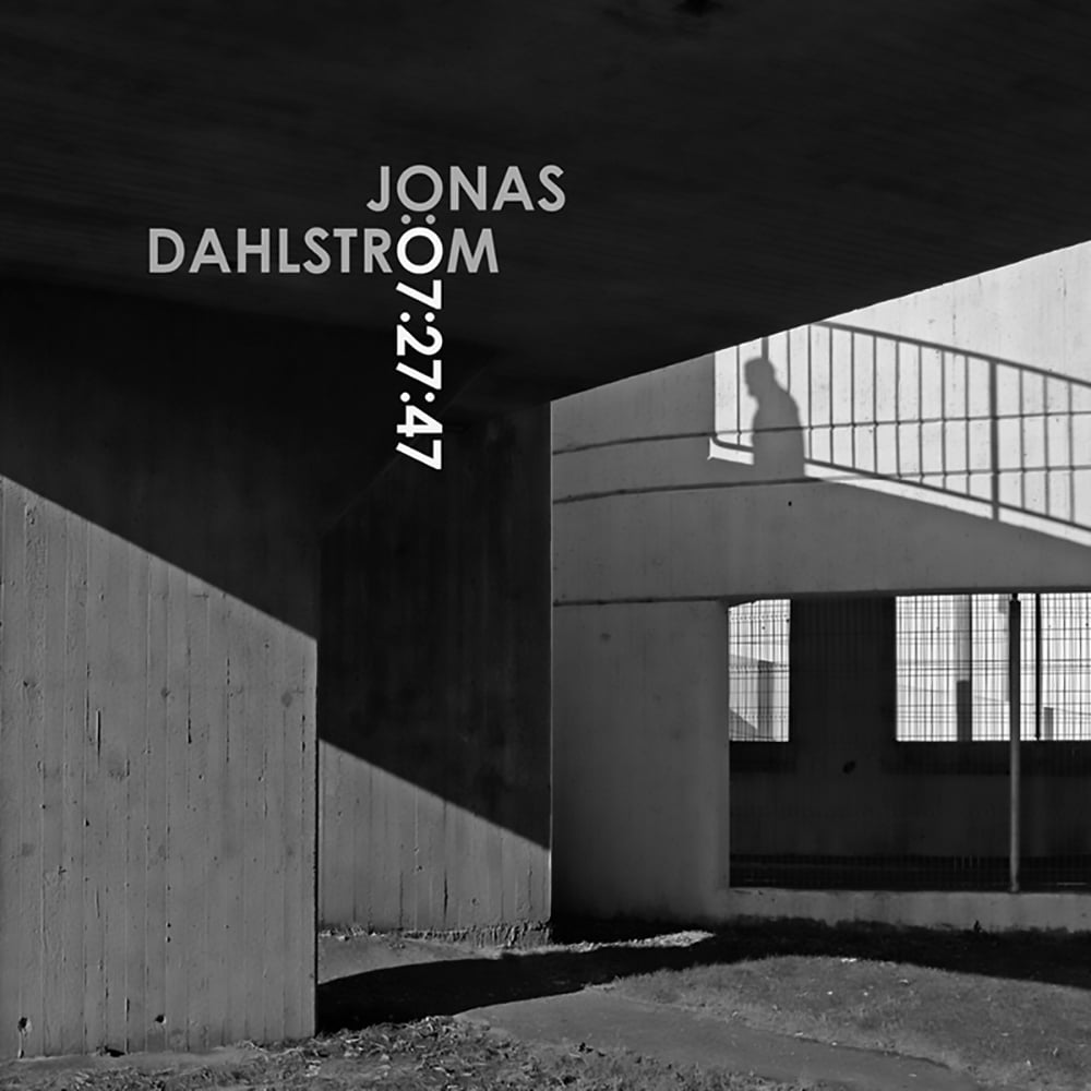 Black and white shot of lone silhouette of figure walking near railings, around brutalist architecture, JONAS DAHLSTRÖM 07:27:47 in grey and white font to upper left.