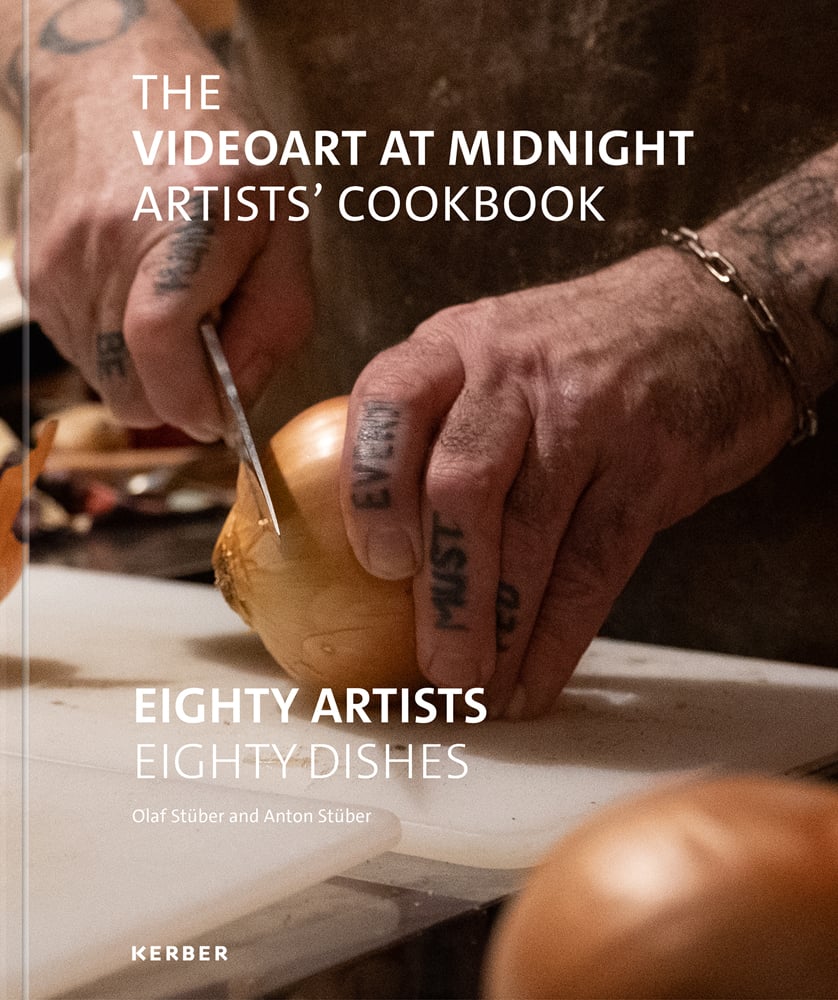 Masculine tattooed hands chop an onion on board with knife with The Videoart at Midnight Artists’ Cookbook in white font above