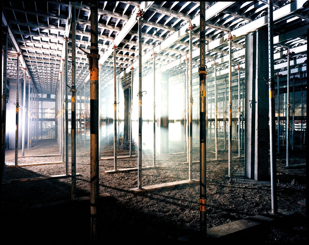 Photo of skeletal inside of cigarette factory during its construction with eerie shafts of light beaming through
