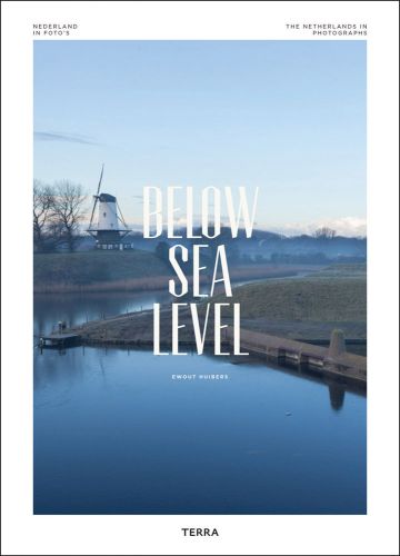 Windmill standing on the edge of river bank, on white cover of 'Below Sea Level, The Netherlands in Photographs', by Lannoo Publishers.