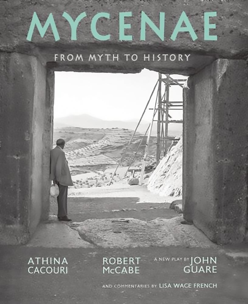 Gigantic concrete entrance with man in suit, holding hat, staring out toward Greek landscape, MYCENAE FROM MYTH TO HISTORY in mint green and white font above.