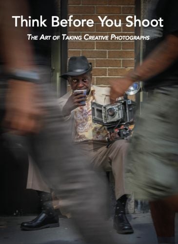 Black man in trilby, sitting in street, holding cup to lips, with old box camera, blurred figures to front, Think Before You Shoot in white font above