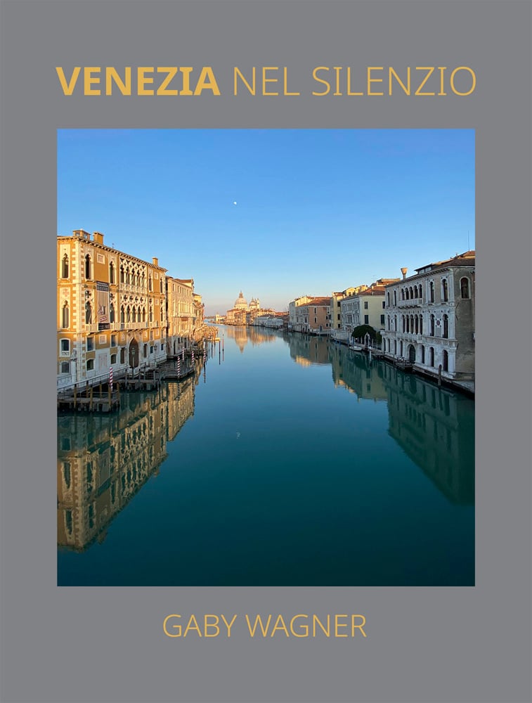 Serene landscape photograph of Venice's canal, beneath blue sky, on grey cover, VENEZIA NEL SILENZIO GABY WAGNER in gold font above and below.