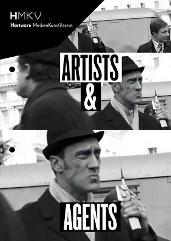 Black and white video still of white male in black hat, holding a silver walkie talkie, ARTISTS & AGENTS in black and white font on white and black banners above and below.
