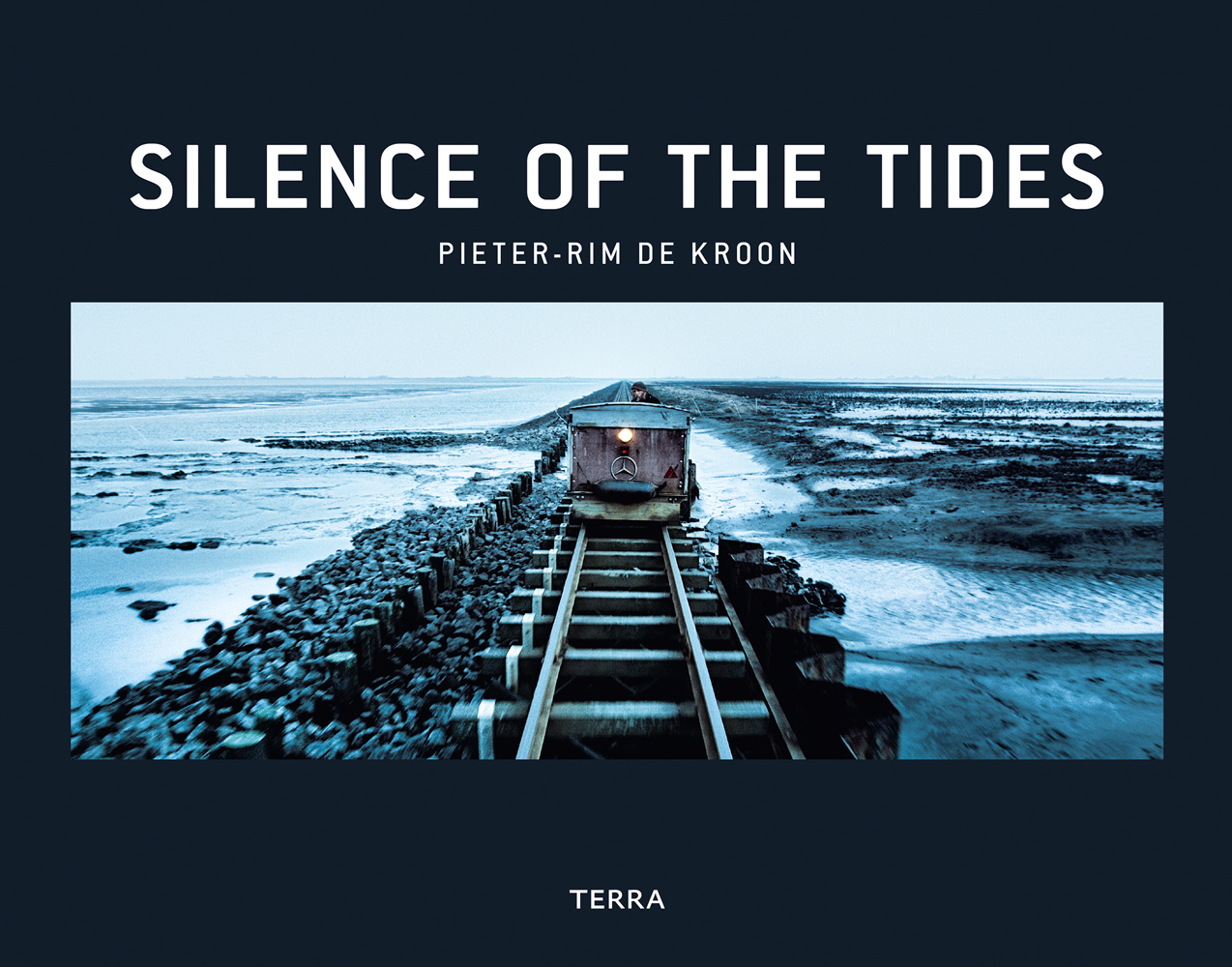 Rail road and embankment on Wadden Sea, wagon with lamp on front, on black cover of 'Silence of the Tides', by Lannoo Publishers.