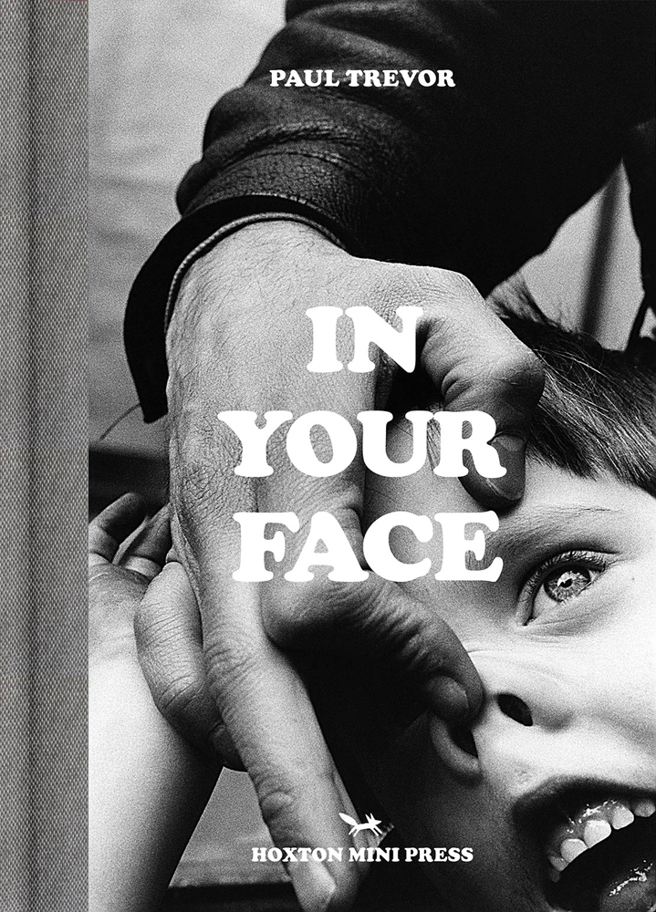Portrait of young white boy having nose pushed up like a pig by another hand, on cover of 'In Your Face', by Hoxton Mini Press.