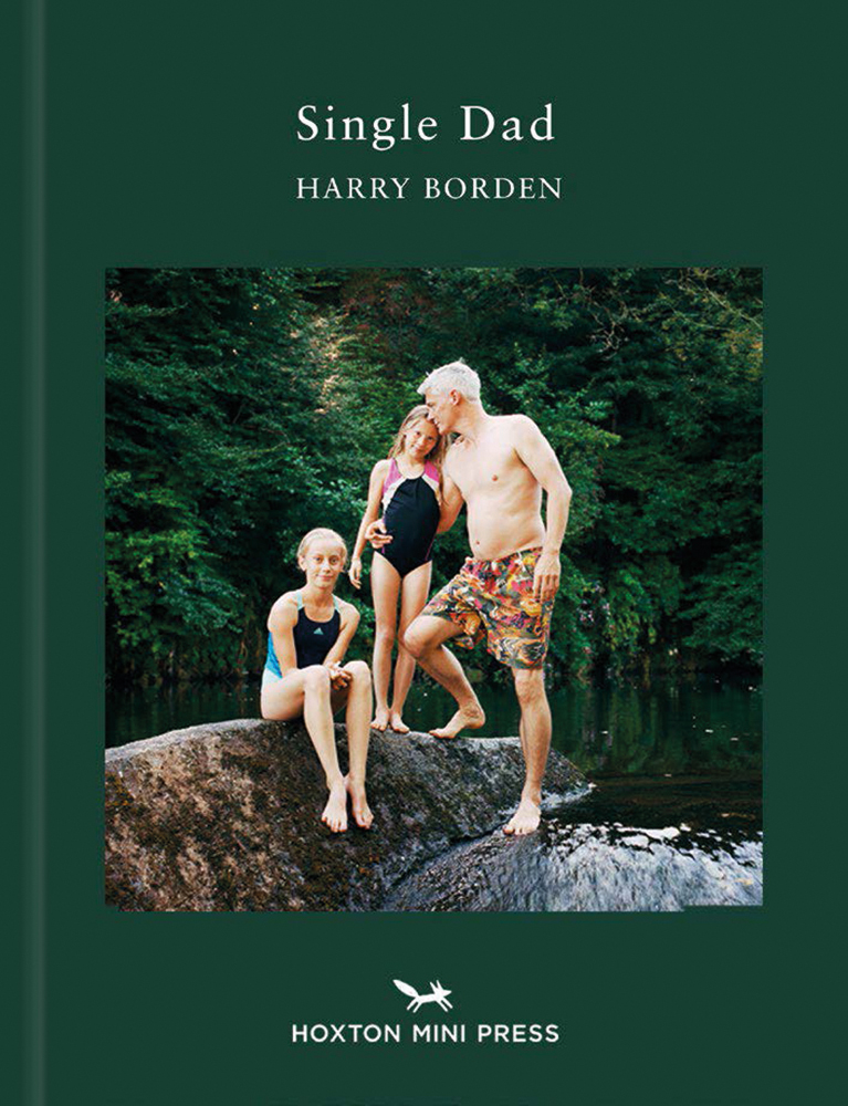 White male with two white children wearing swimming gear, standing on large river rock, on green cover of 'Single Dad', by Hoxton Mini Press.