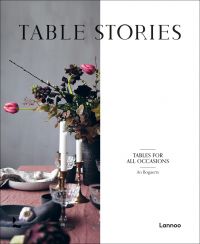 Wood table with vase of flowers, candlesticks, glasses and bowls, on cover of 'Table Stories, Tables for All Occasions', by Lannoo Publishers.