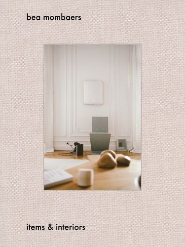 Interior living space with wood table, white walls, on pale pink woven cover, of 'Bea Mombaers, Items & Interiors', by Luster Publishing.