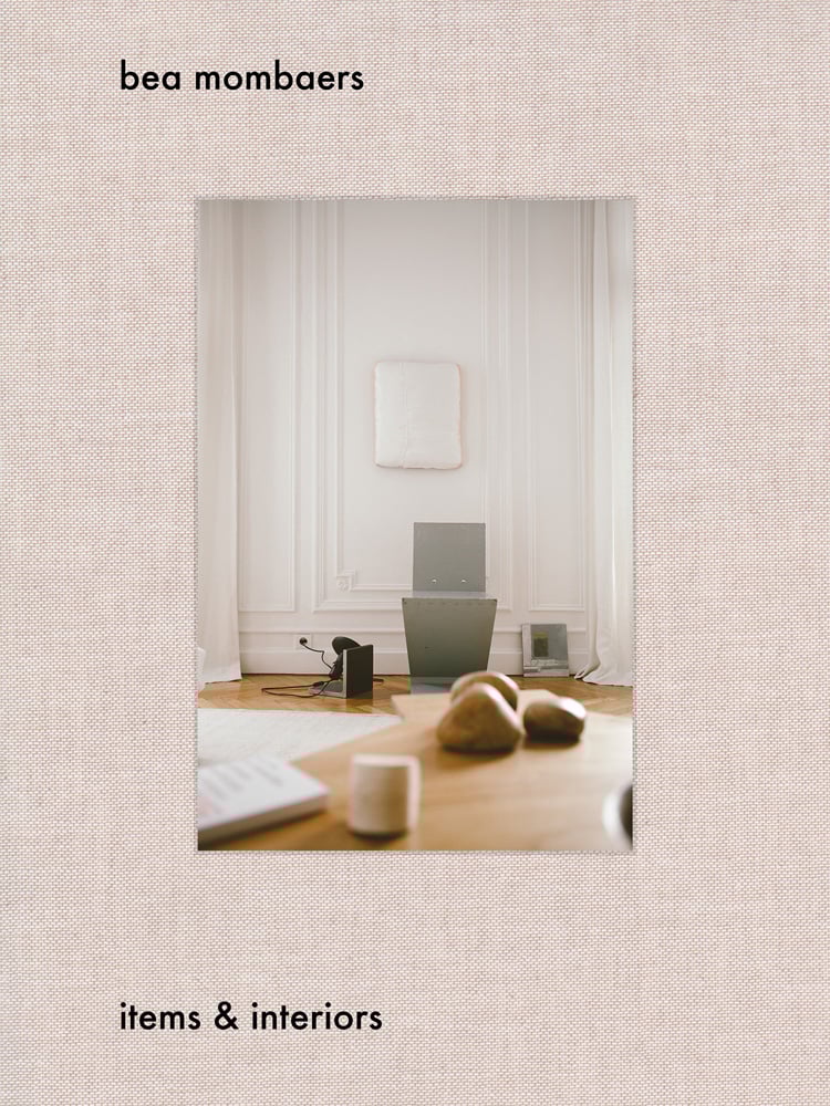 Book cover of Bea Mombaers, Items & Interiors, with interior living space with wood table, white walls. Published by Luster Publishing.
