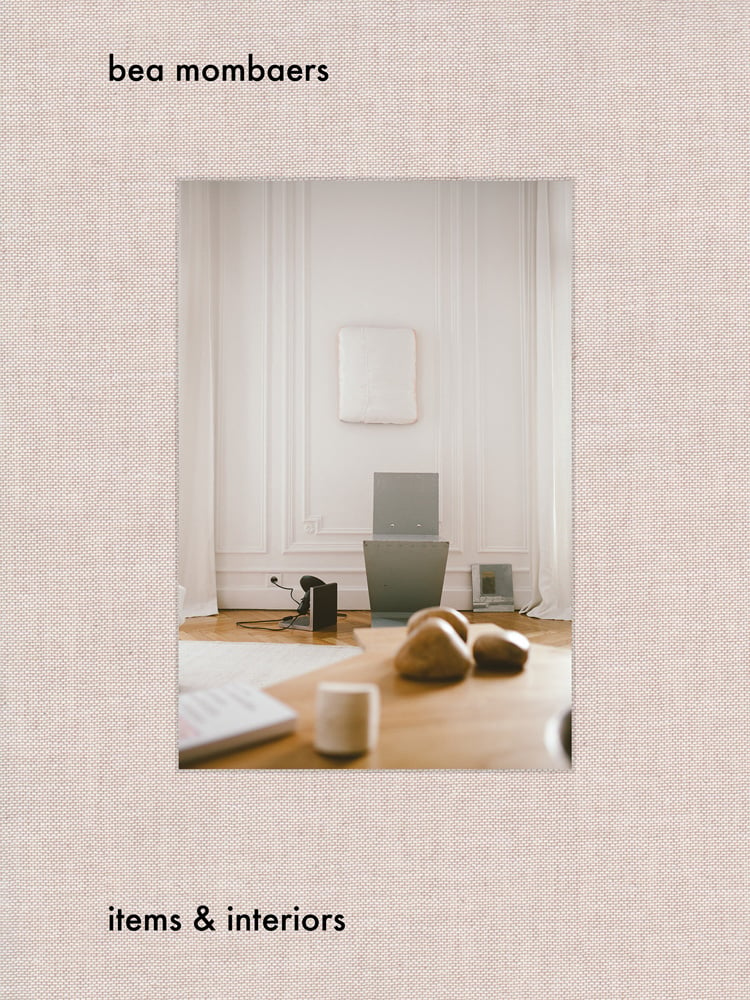 Interior living space with wood table, white walls, on pale pink woven cover, of 'Bea Mombaers, Items & Interiors', by Luster Publishing.