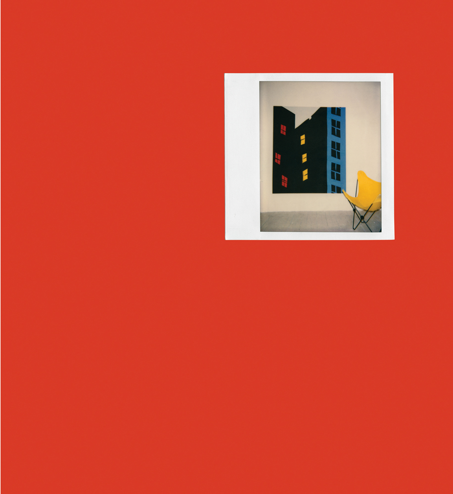 Polaroid of pop art inspired painting of high rise building on wall, yellow chair to right, on red cover