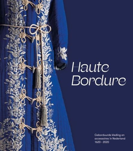 Section of long bright blue coat with floral gold embroidery and tasselled belt with dark blue backdrop and Haute Bordure in white font