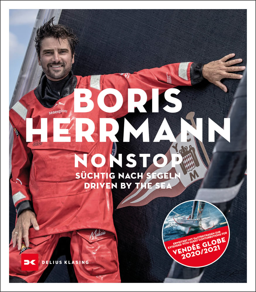 Boris Hermann smiling while on boat in red waterproofs holding back sail with one hand, on cover of 'Nonstop, Süchtig nach Segeln / Driven by the sea', by Delius Klasing Verlag GmbH.