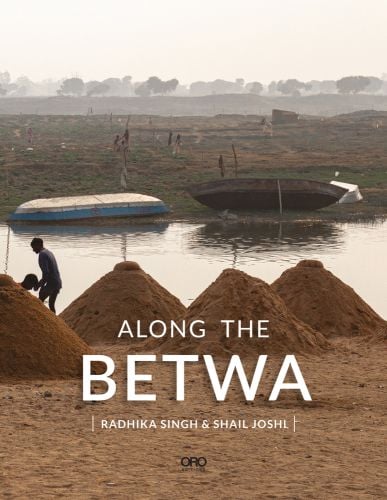 Piles of sand heaped by side of Betwa river with fishing boats on opposite side and Along the Betwa in white font below