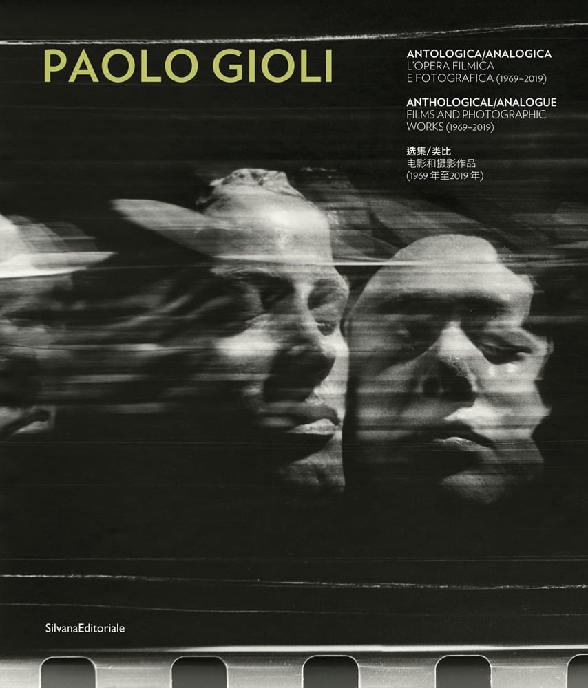 Blurred, grainy black and white photo of 2 faces touching, with eyes closed and Paolo Gioli in yellow font above