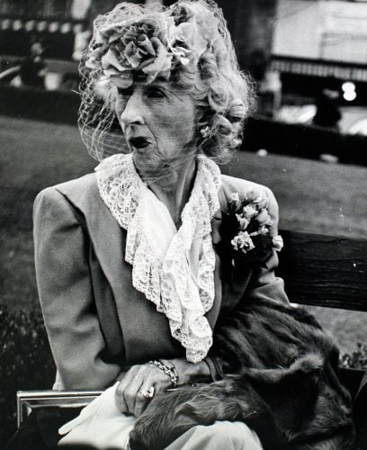 Pouting female in floral fascinator, holding clutch bag, with fur coat under arm