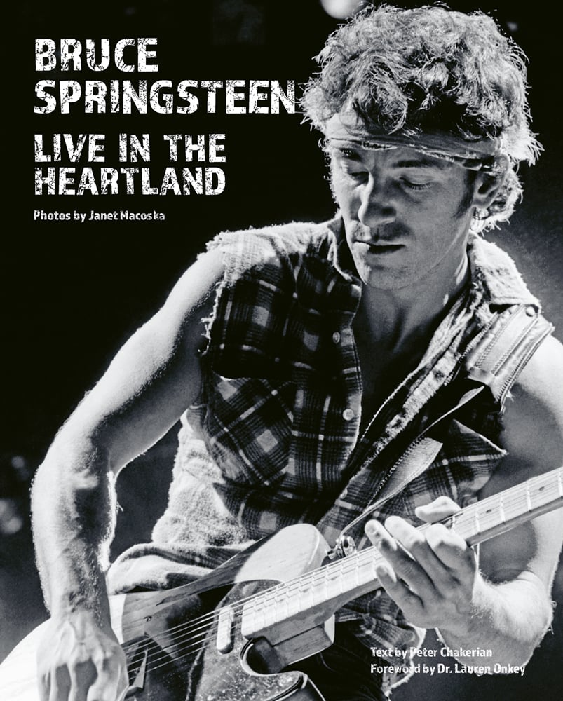Bruce Springsteen wearing bandana, playing electric guitar on stage, on cover of 'Bruce Springsteen Live in the Heartland Photos by Janet Macoska', by ACC Art Books.