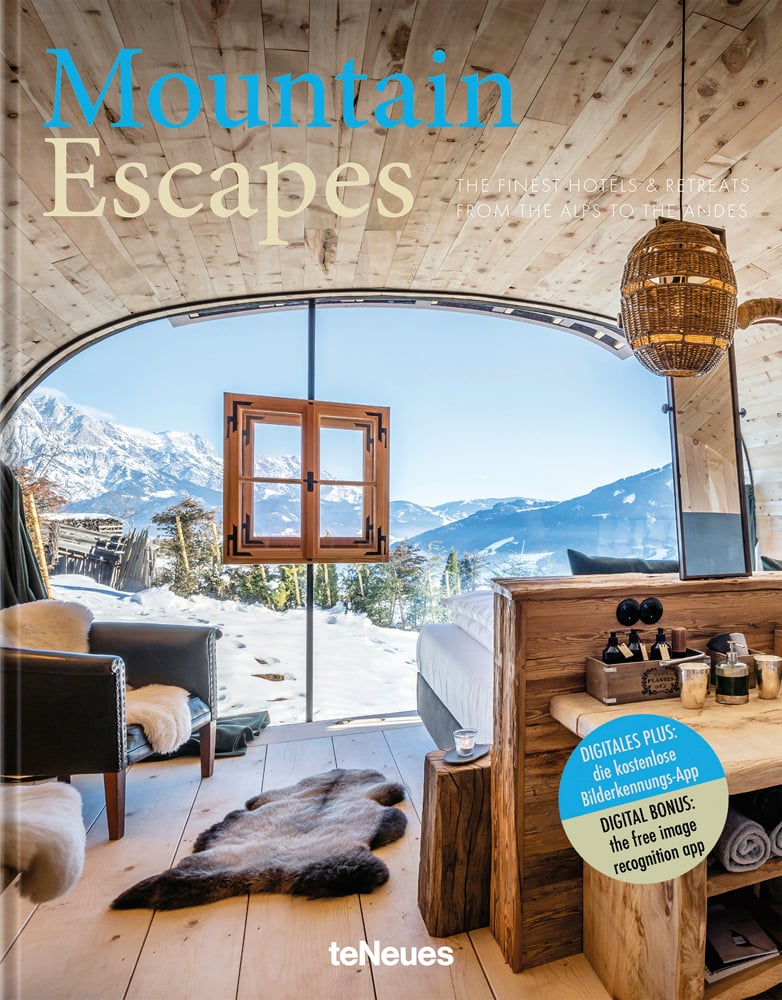 Book cover of Mountain Escapes: The Finest Hotels and Retreats from the Alps to the Andes, featuring the interior of wood chalet with views of snow-topped mountains. Published by teNeues Books.