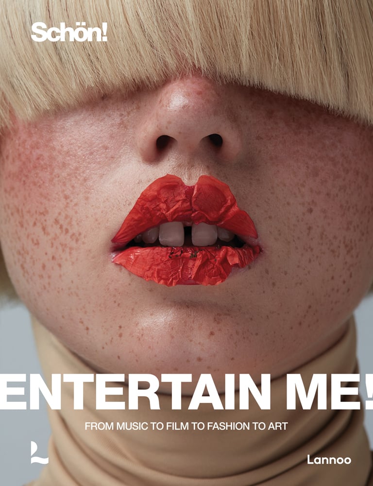 Model with freckled face, blonde fringe covering eyes and orange petals on lips, on cover of 'Entertain me! by Schön magazine, From music to film to fashion to art', by Lannoo Publishers.