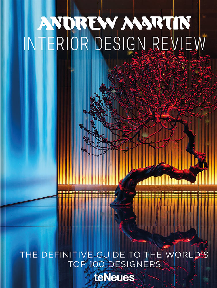 Interior space with twisted tree trunk, illuminated red, wall of blue light to left, 'ANDREW MARTIN INTERIOR DESIGN REVIEW', in white font above.