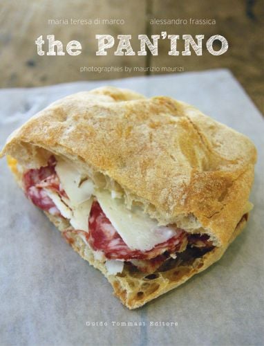 Sliced portion of salami and cheese panini on baking paper with the PAN'INO in white stencilled font