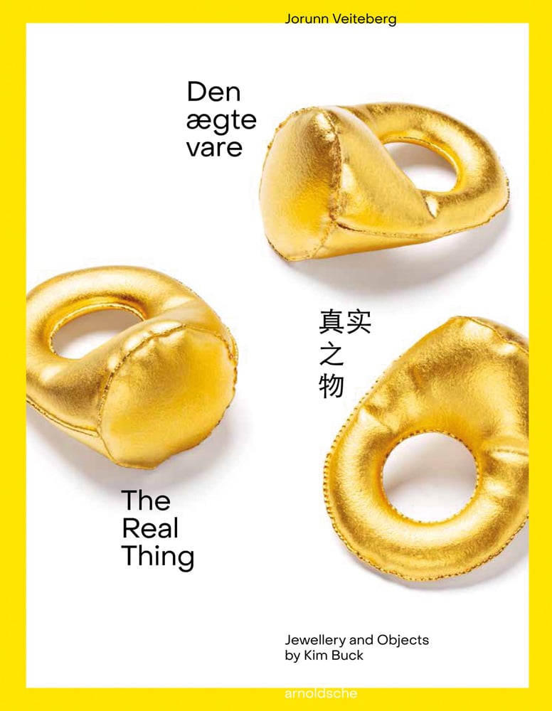 Three gold rings made from shiny fabric with stuffing, on white cover of 'The Real Thing Jewellery and Objects by Kim Buck', by Arnoldsche Art Publishers.