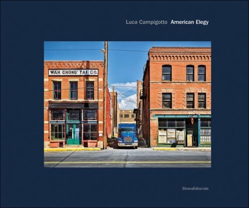 Blue juggernaut parked between brick buildings on American street with Luca Campigotto American Elegy in white font on blue cover