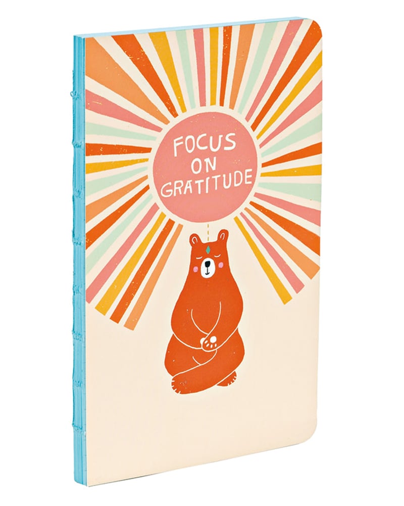 Bright brown illustration of bear meditating with lighter orange circle above with coloured strokes emanating with Focus on Gratitude in centre in white font