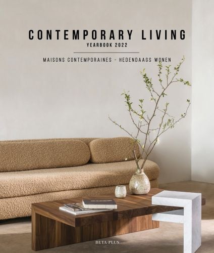 Interior with fluffy brown sofa, wooden table with foliaged branch in vase and Contemporary Living Yearbook 2022 in black font