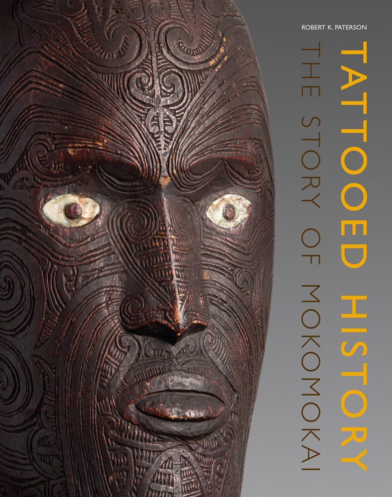 Decoratively carved wood mask on grey cover with Tattooed History in yellow font