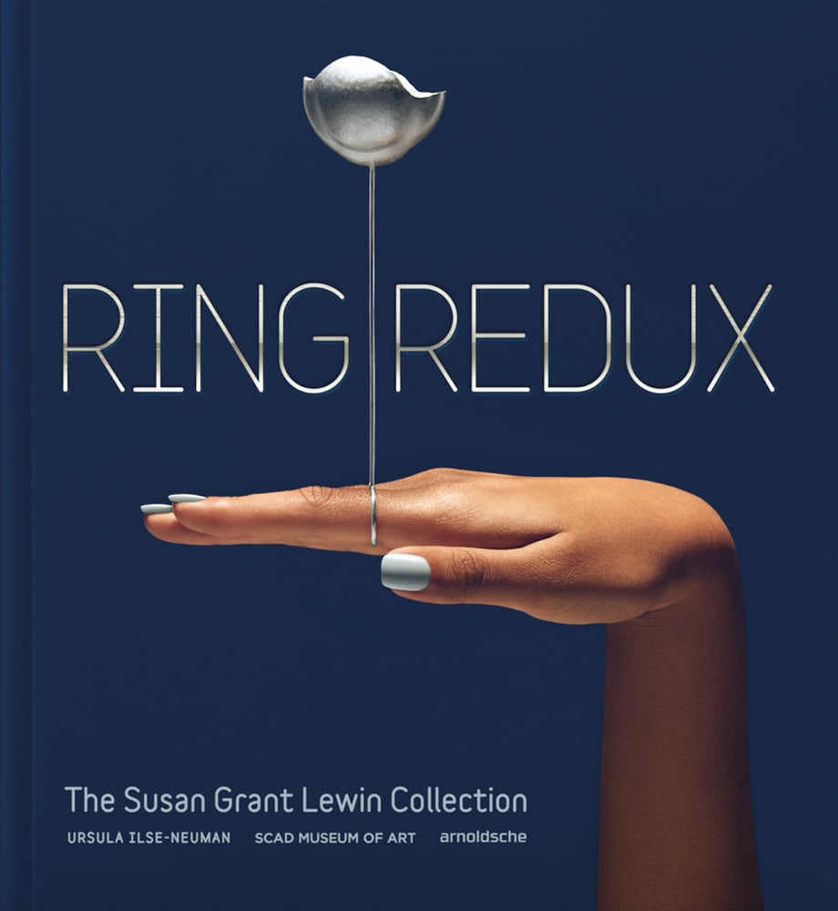 Dark blue cover with hand at 90 degree angle to wrist and silver ring with long stem and flower, on index finger and Ring Redux in silver white font