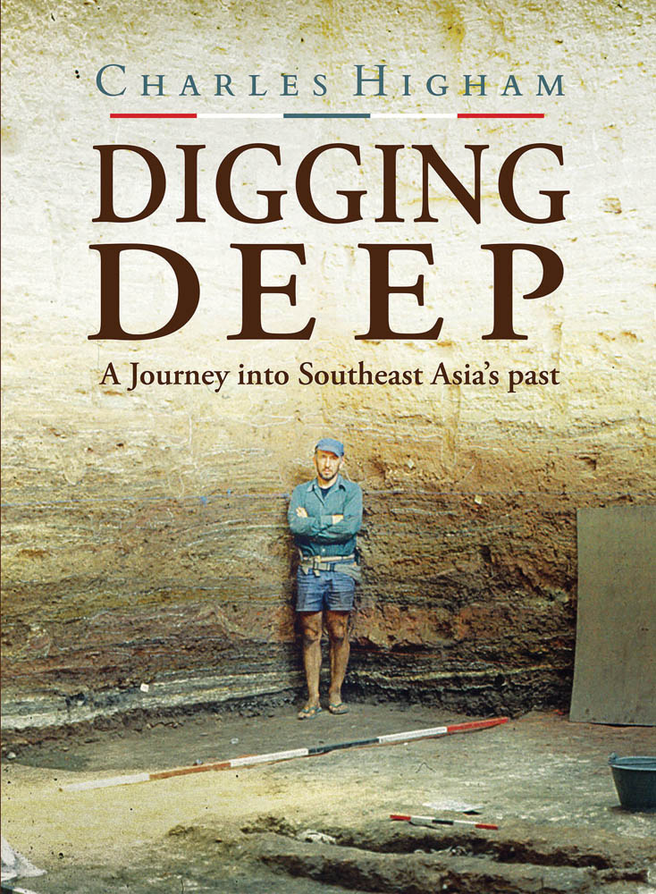 Young Charles Higham in blue shirt and denim shorts, standing in excavated ground, high wall behind, DIGGING DEEP A Journey into Southeast Asia's past in brown font above.