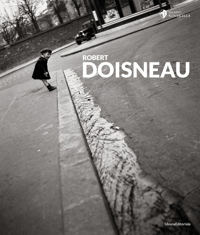 Black and white photo of child by side of road leaning forward to look at water running down road with Robert Doisneau in white font