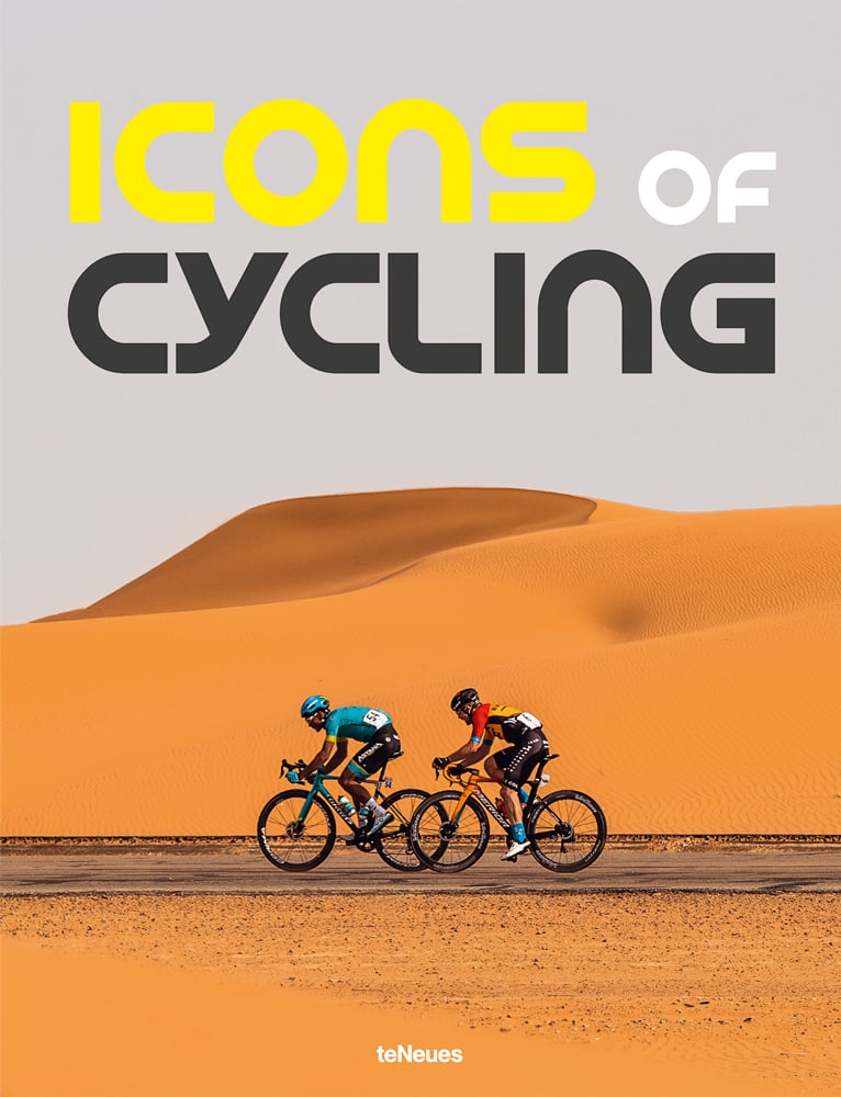 Two road racing bikers cycling on road with sand hills in the background and Icons of Cycling in yellow white and grey font above